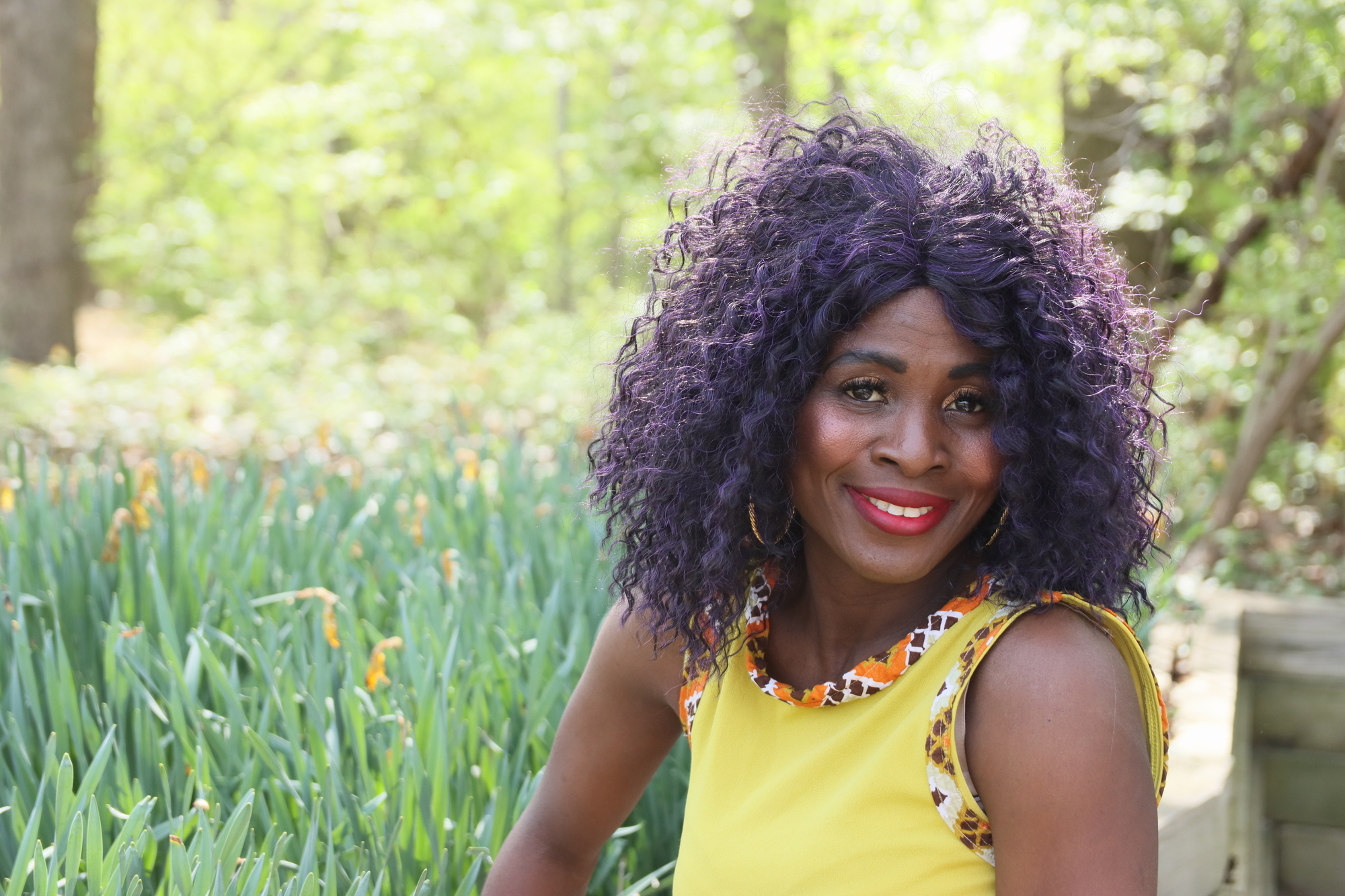 dark skinned woman in bright yellow colored dress smiles in a field of green